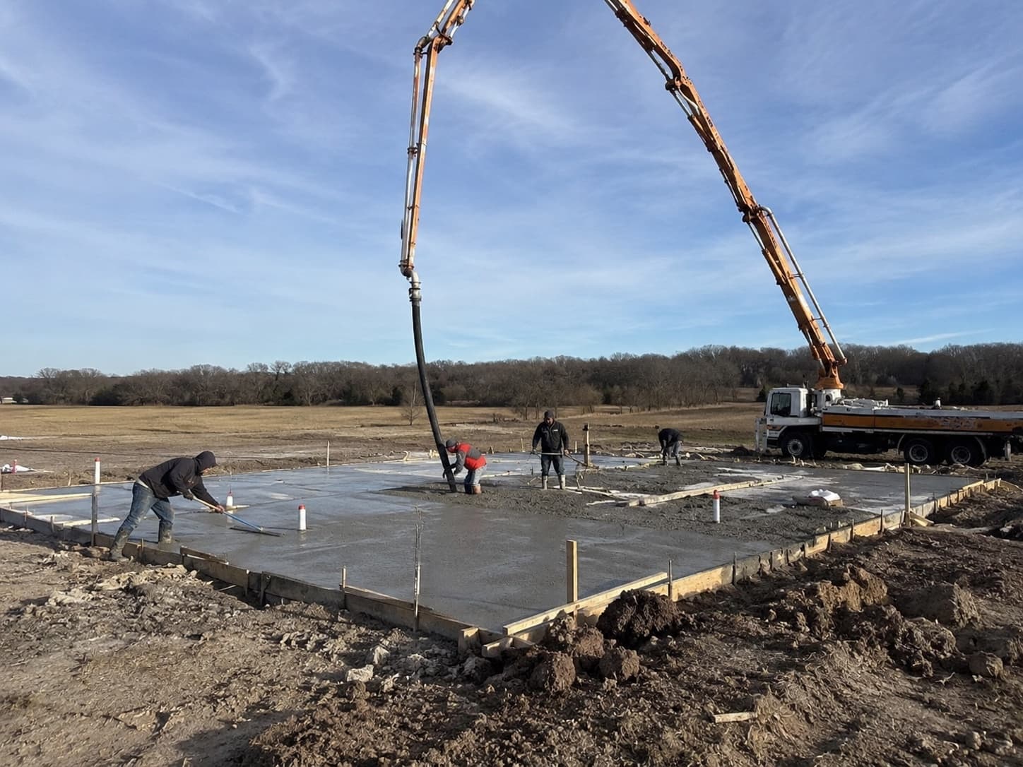 Boom pump truck placing concrete for a residential slab foundation on a North Texas lot while the crew screeds and floats the wet slab